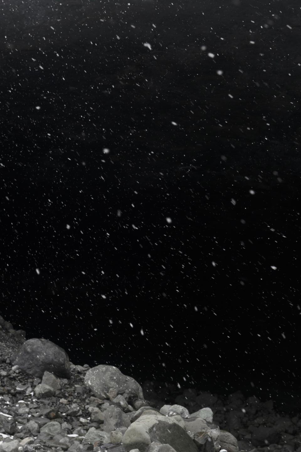 Snow moves diagonally through a field of black.
The falling white carries a faintly cosmic scale.
